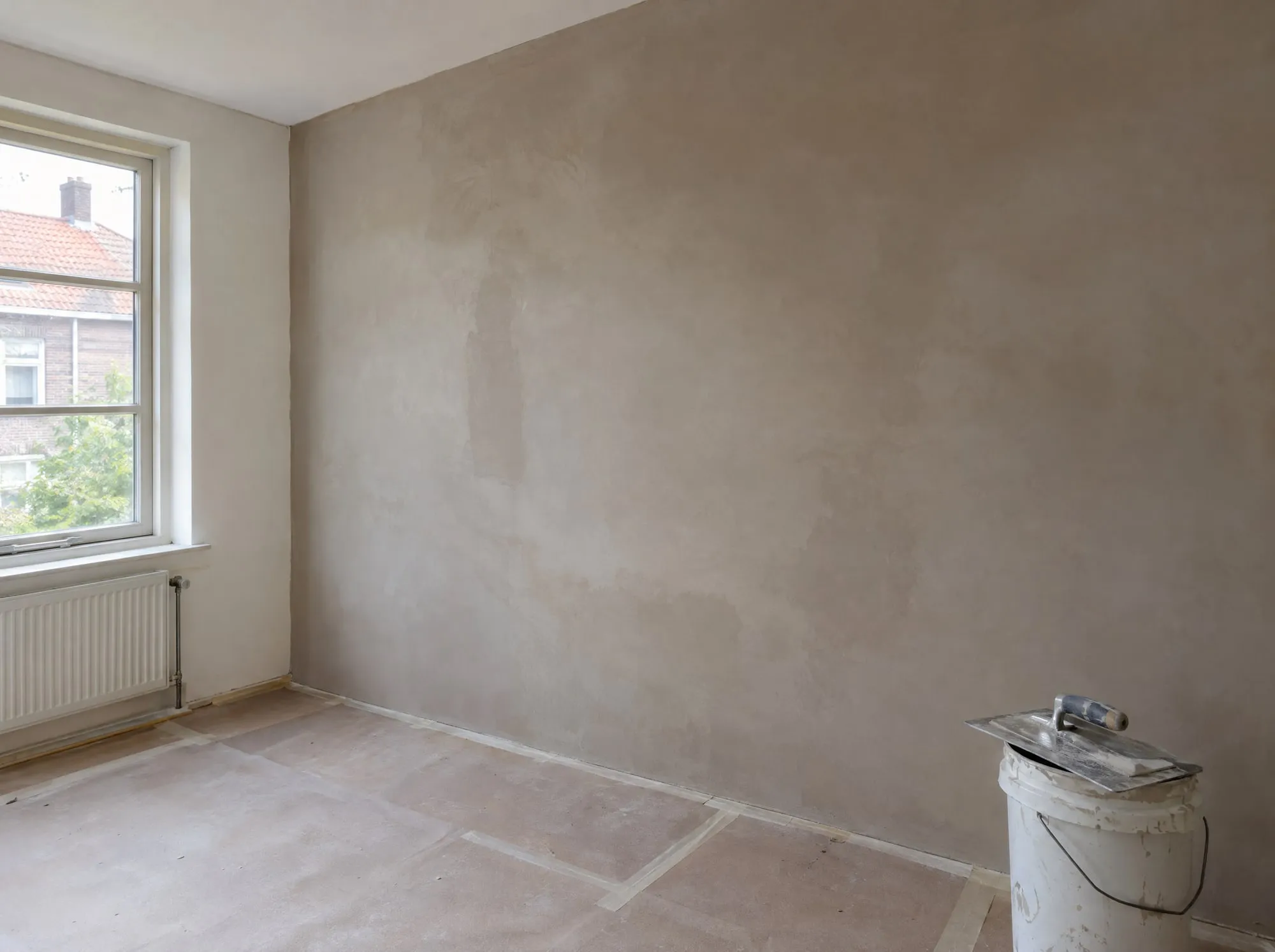 Vers gestucte muur die nog droogt, met stucgereedschap op een emmer